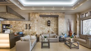 A modern lobby with a stone wall, a reception desk, two sofas, and a coffee table. - Elotis Suites (Chania)