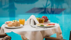 A dining table with breakfast items including croissants, fruit, and juice, near a pool. - Elotis Suites (Chania)