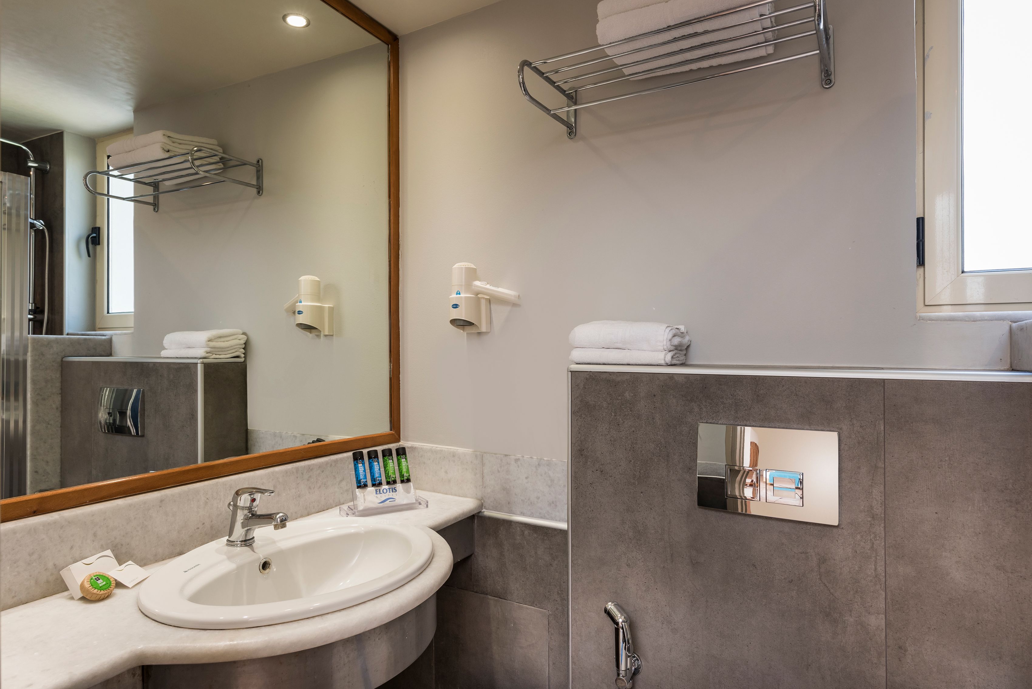 A modern bathroom with a large mirror, two sinks, a towel rack, and a shower area.