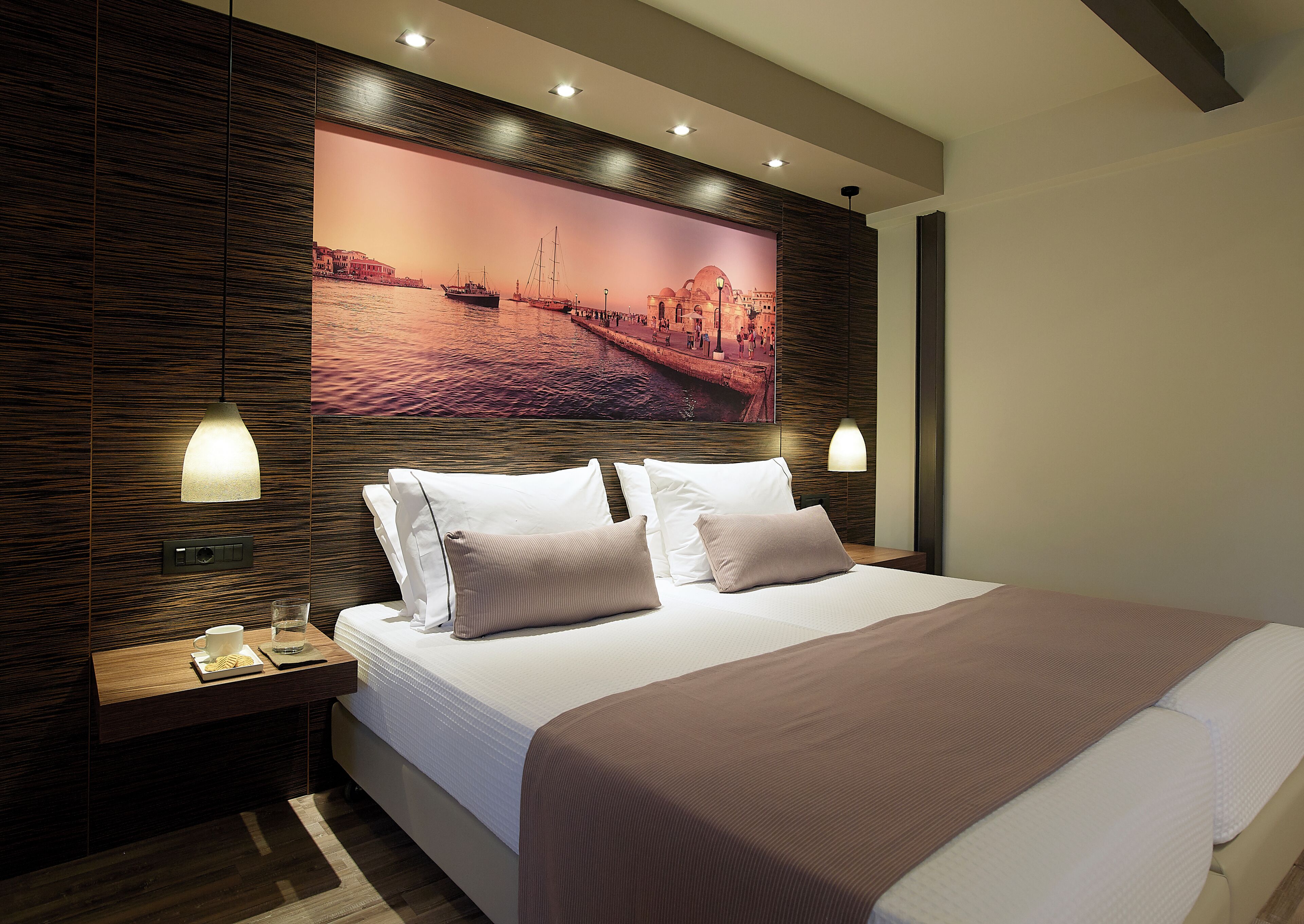 Una habitación de hotel moderna con una cama grande, dos mesitas de noche, una lámpara de pared y un cuadro panorámico de gran tamaño.
