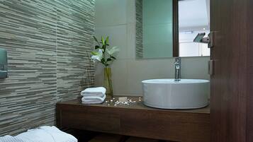 Un baño moderno con inodoro, lavamanos y espejo. Hay toallas y un florero con flores en la encimera.