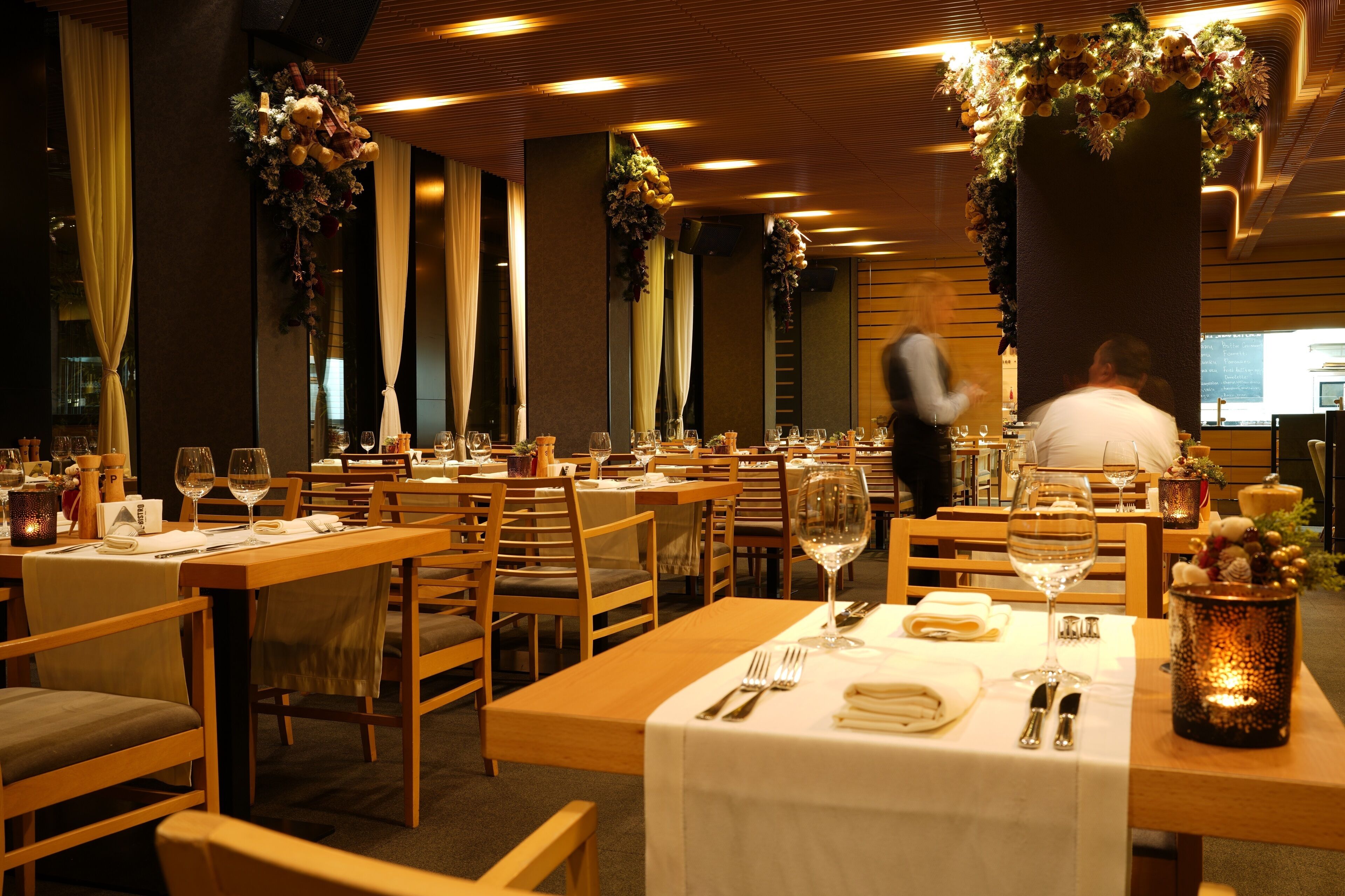 A restaurant with wooden tables and chairs, white tablecloths, and floral decorations.