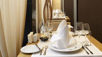 Mesa de comedor de hotel con mantel blanco, cubertería y copas de vino, que sugiere una experiencia gastronómica formal.