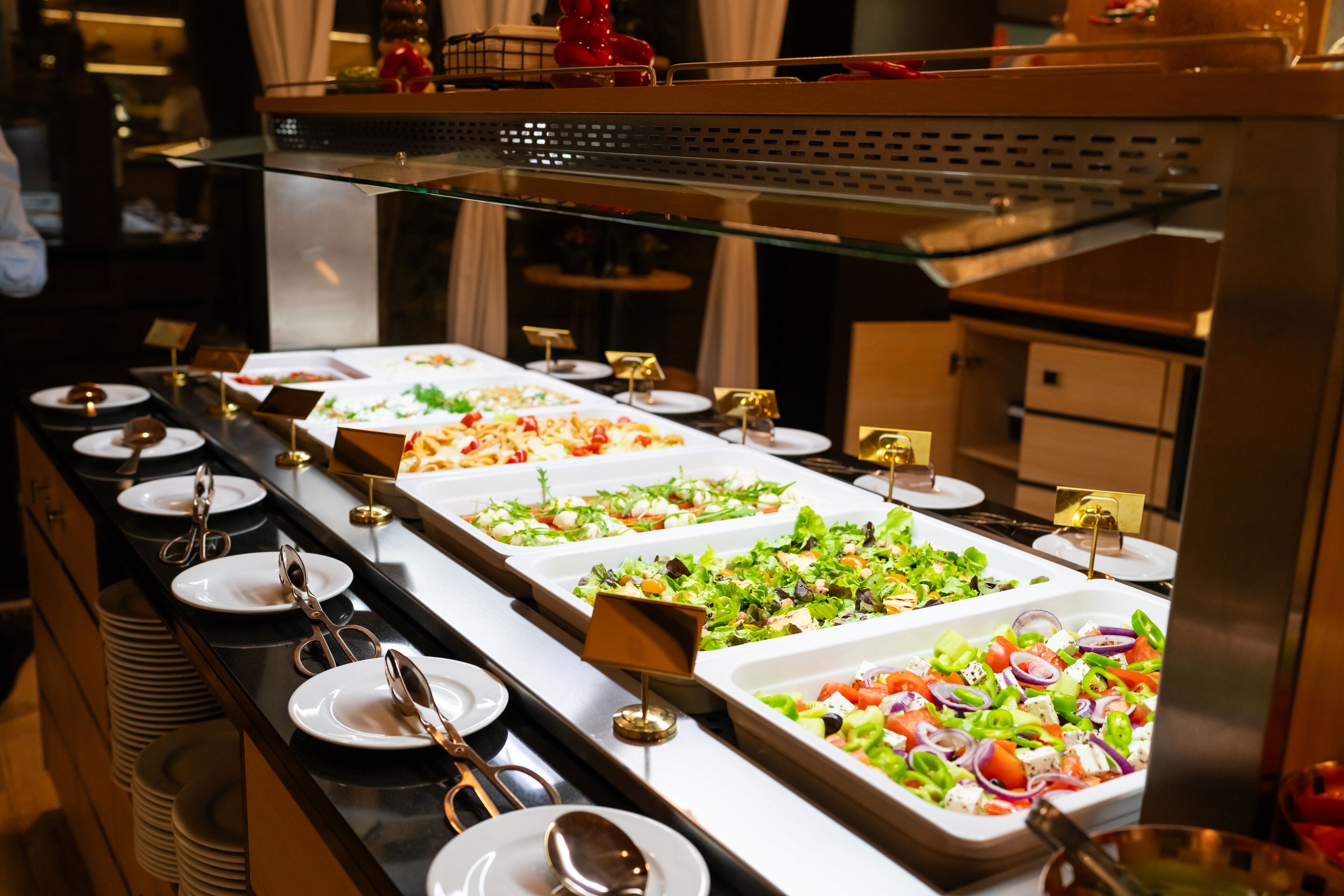 Ein Buffet mit verschiedenen Speisen, darunter Salate und andere Gerichte, auf einem langen Tisch mit Tellern und Besteck.
