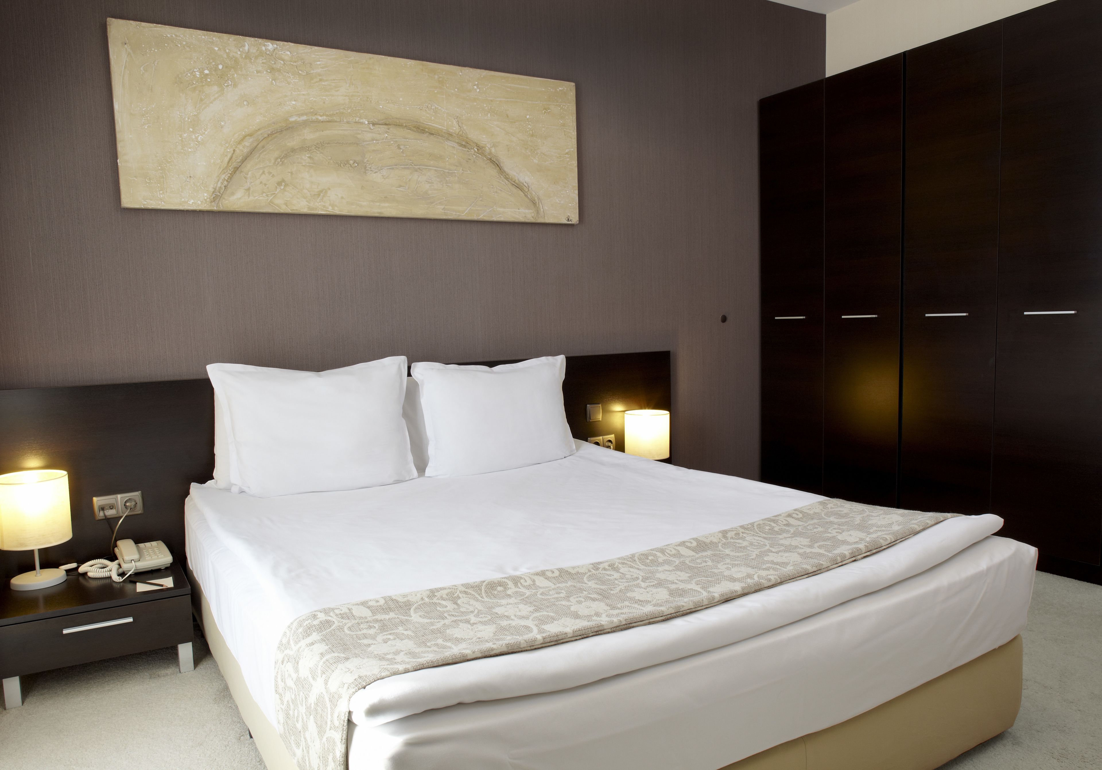 A neatly made bed with white linens, a bedside lamp, and a telephone on a nightstand.