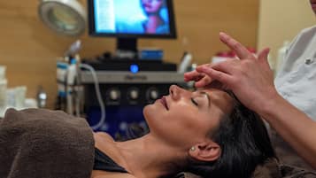 A person lying down with a medical device attached to their head, a monitor in the background, and a person standing beside them.