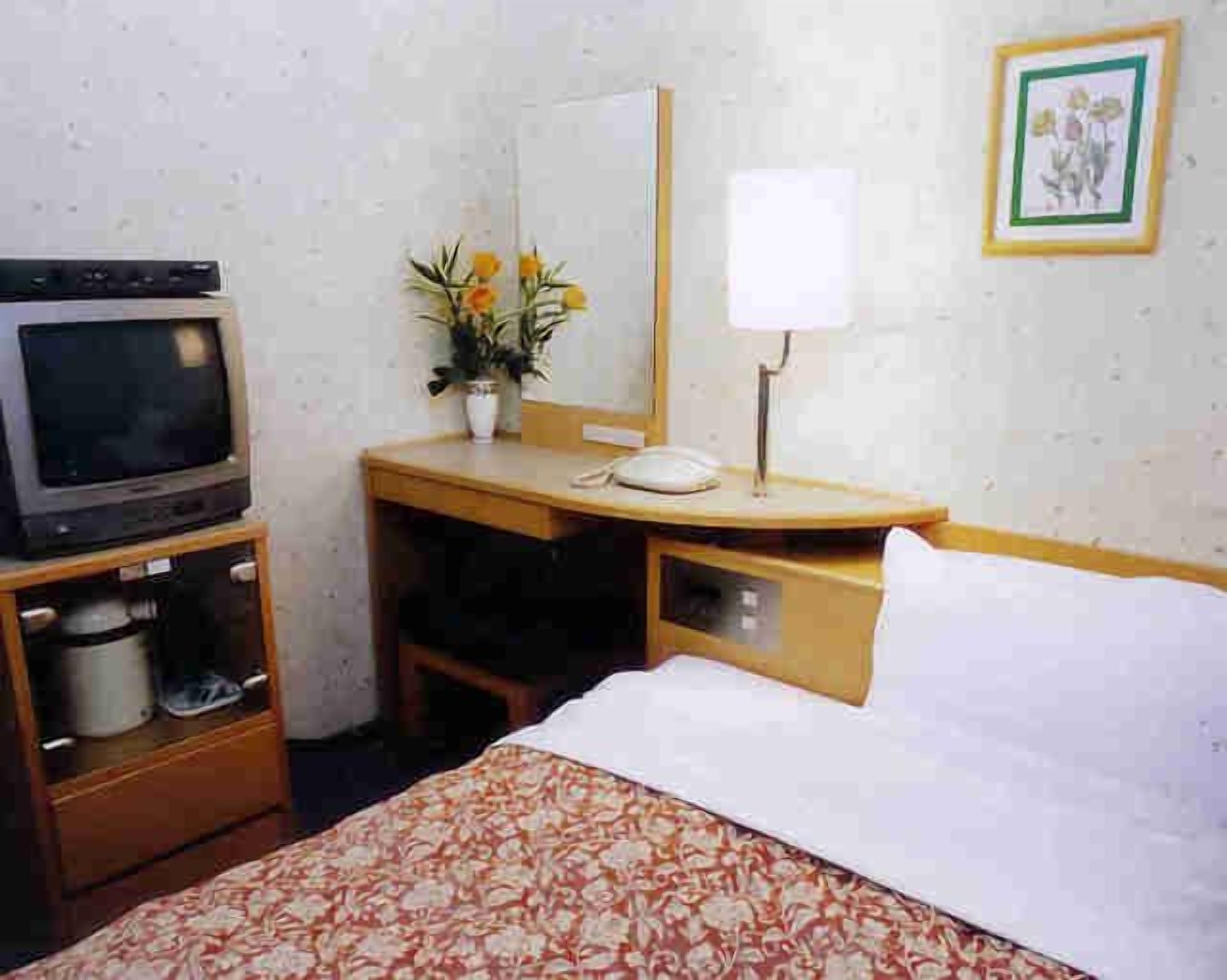 Et hotelværelse med seng, skrivebord med telefon, fjernsyn og spejl.