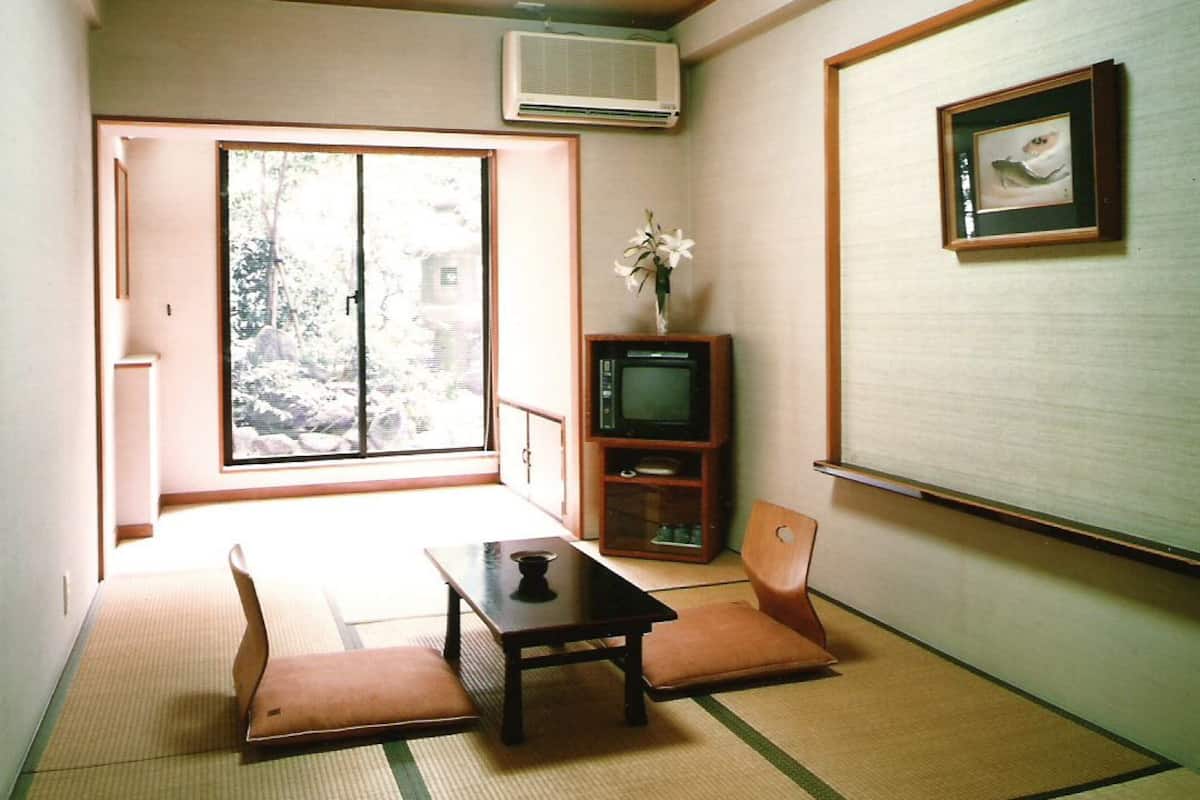 Une pièce de style japonais traditionnel, avec un sol recouvert de tatamis, une table basse, un téléviseur posé sur un meuble et un tableau encadré accroché au mur.