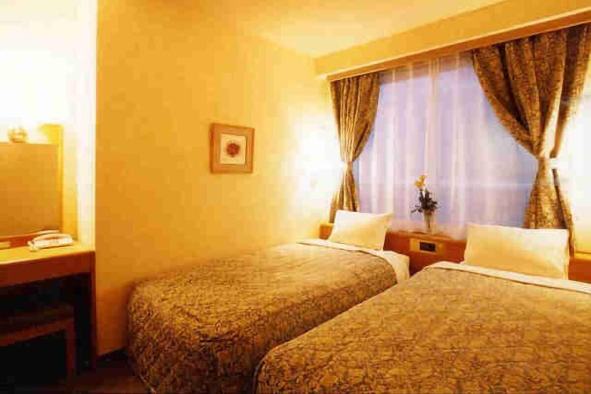 Quarto de hotel com duas camas, uma mesa, um telefone e um quadro na parede.