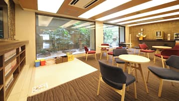 A modern interior with a large window, wooden bookshelves, and a seating area with tables and chairs.