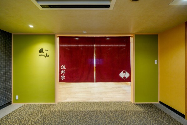 Ein Hotelzimmer-Eingang mit roter Tür, grünen Wänden und einem gemusterten Teppich.