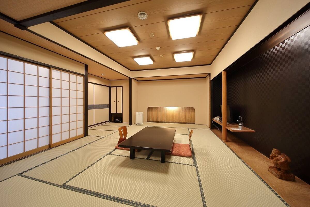 Ein traditioneller japanischer Raum mit Tatami-Boden, einem niedrigen Tisch, Schiebetüren und einer dunklen Wand mit Schachbrettmuster.