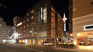 A multi-story hotel with illuminated signage, a parking area, and a street view at night. - Kyoto Hotel SANOYA (Kyoto)