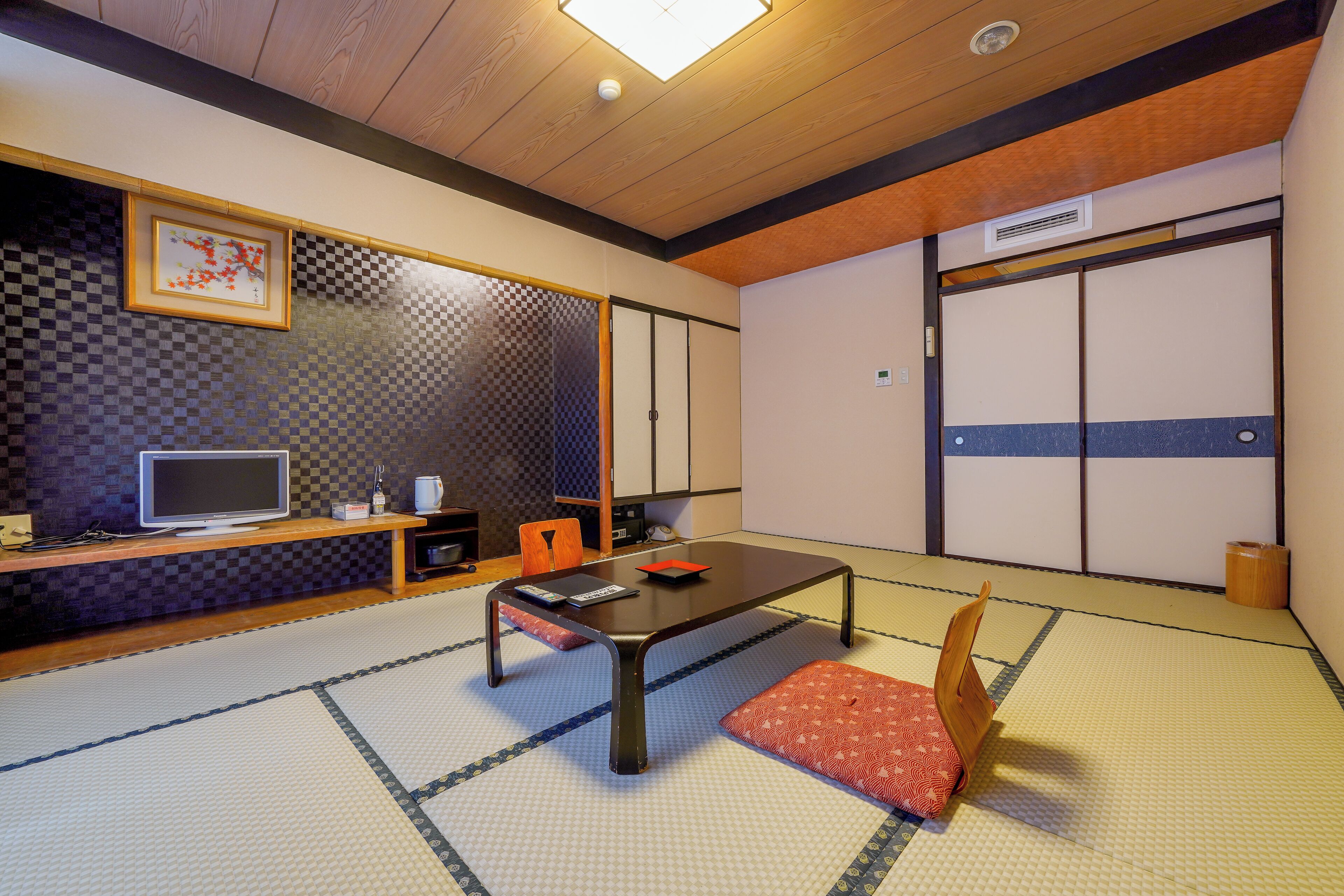 Una habitación japonesa tradicional con suelo de tatami, una mesa baja, un televisor y puertas correderas.
