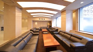 A modern lounge area with leather sofas, a long wooden table, and a large window providing a view of the city. - Kyoto Hotel SANOYA (Kyoto)