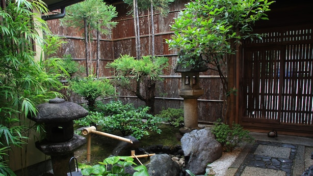 Un jardín japonés tradicional con valla de madera, faroles de piedra y diversas plantas.