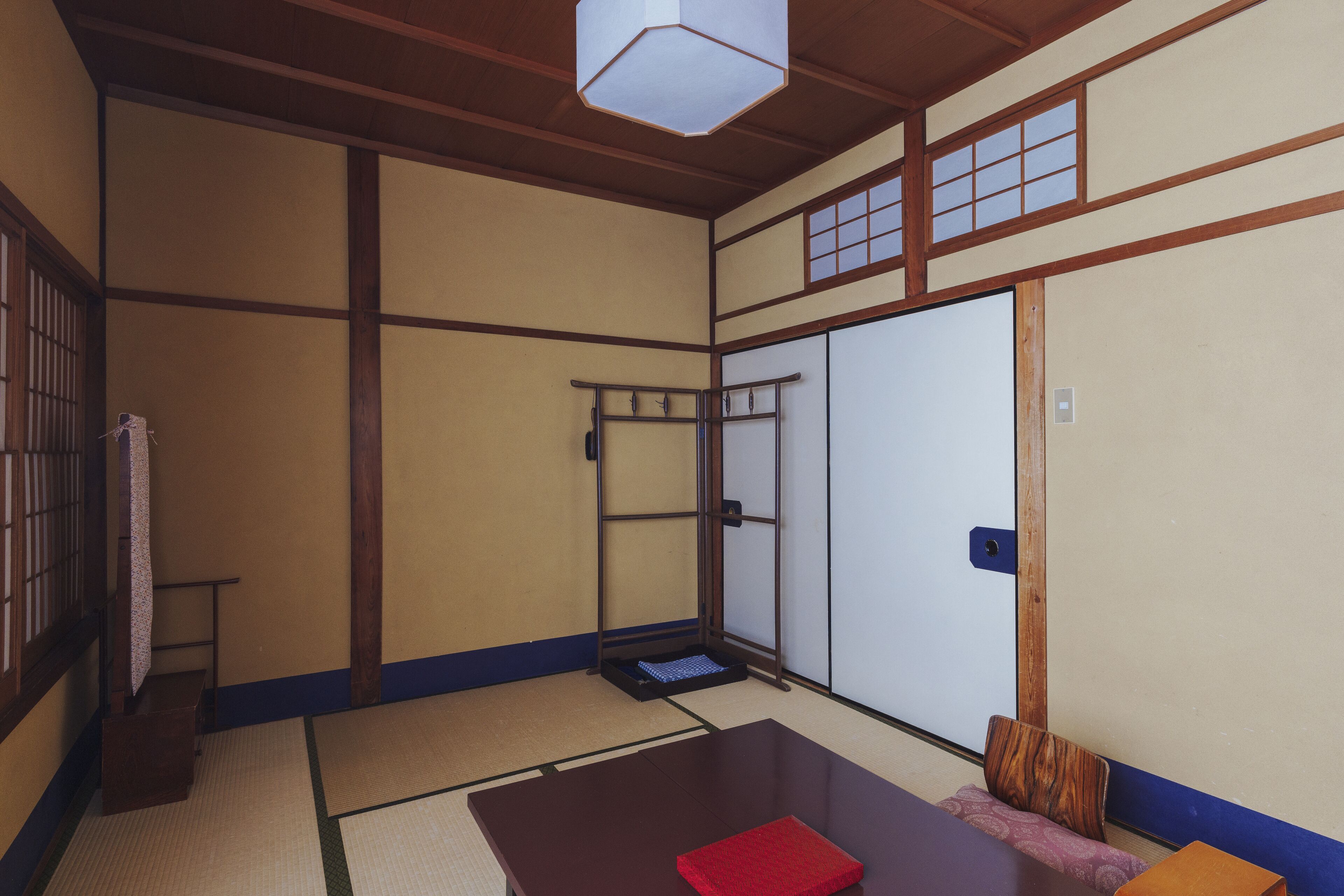 A traditional Japanese room with tatami flooring, a low table with a red mat, a wooden bench, and a sliding door.