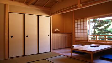 Una habitación japonesa tradicional con suelo de tatami, puertas correderas, una mesa baja y vista a un árbol a través de una pantalla shoji.