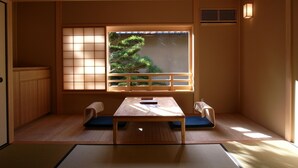 Una habitación japonesa tradicional con suelo de tatami, una mesa baja y una ventana con vistas a un bonsái.