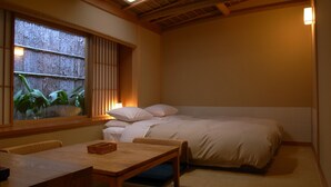 Una habitación con cama, una mesa y ventana con vista a plantas.