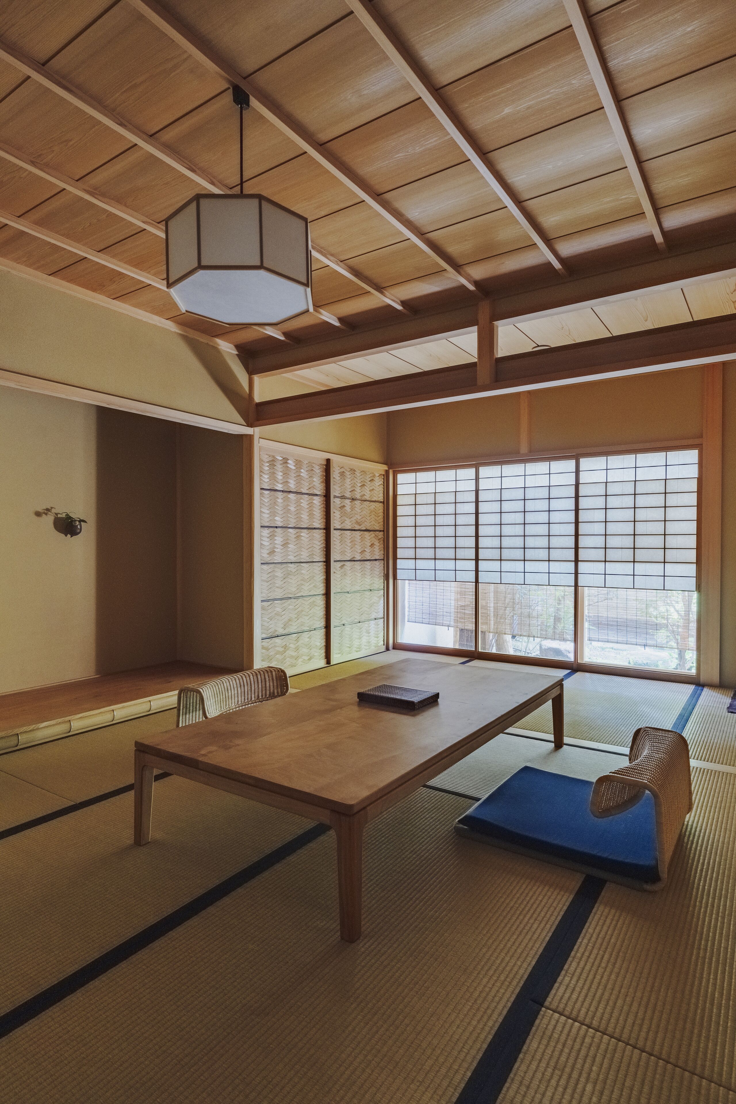 Een traditionele Japanse kamer met tatami vloerbedekking, een lage houten tafel, een blauw kussen, een hanglamp en een shoji scherm.