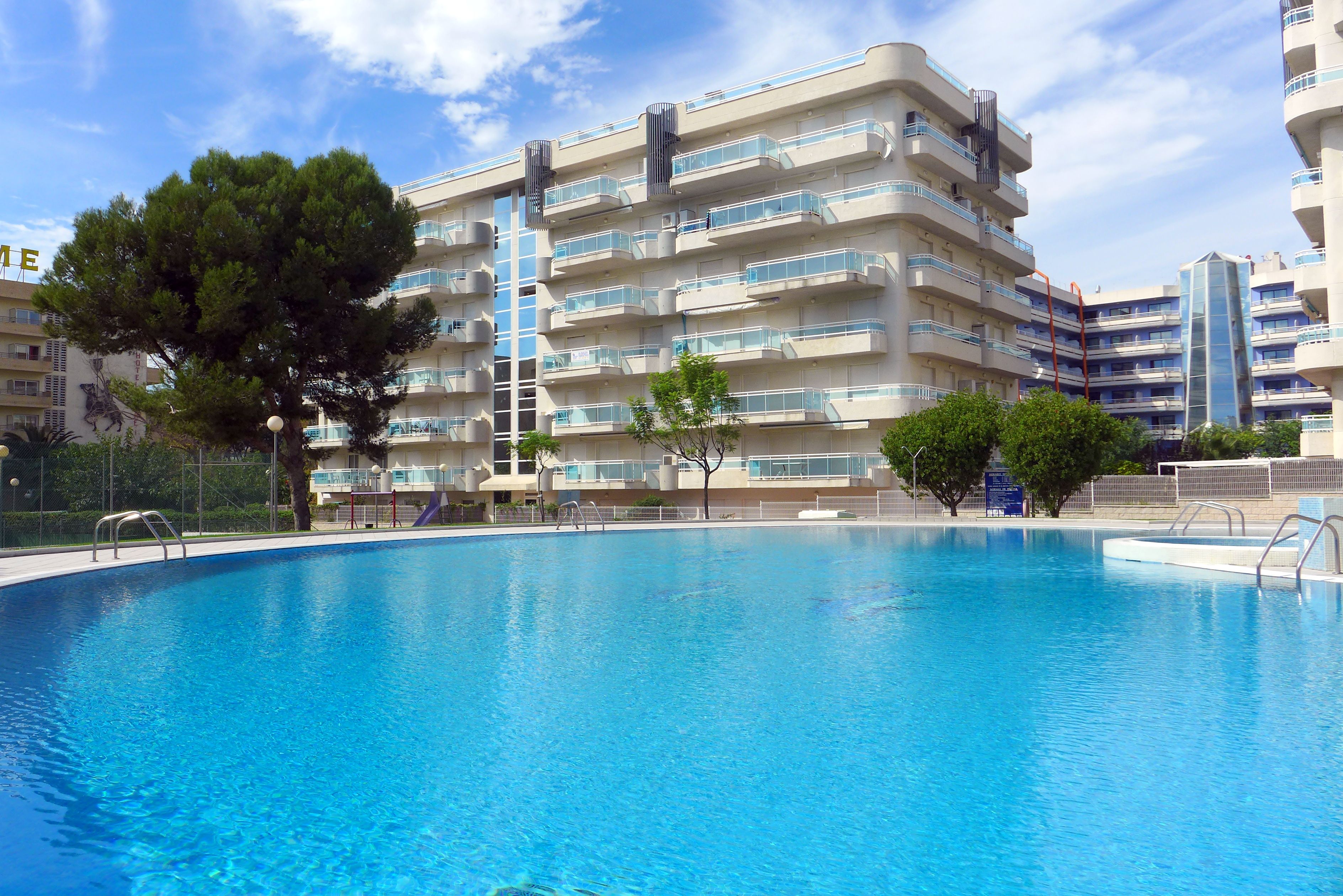 A swimming pool surrounded by multi-story residential buildings with balconies and a clear sky.