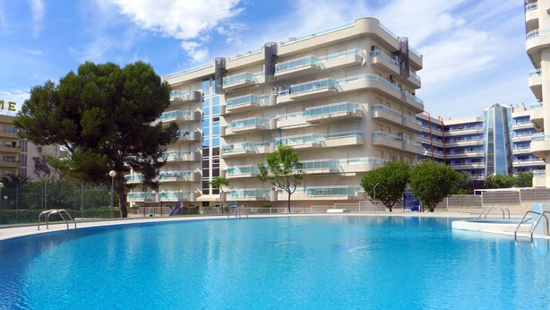 Una piscina rodeada de edificios residenciales de varios pisos con balcones y un cielo despejado.