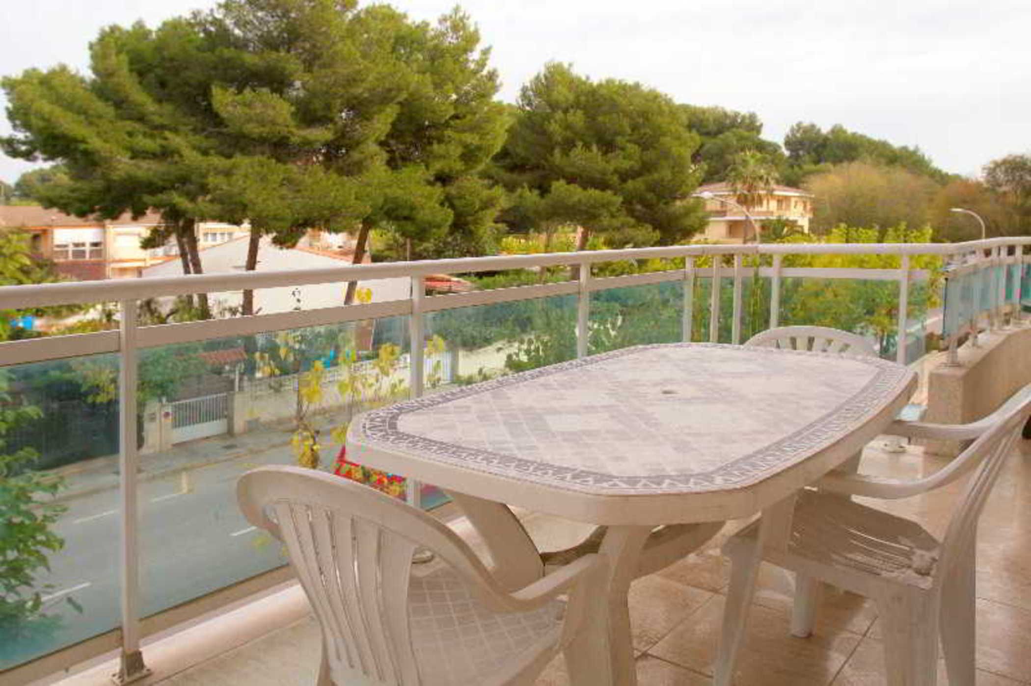 A balcony with a table and chairs, overlooking a street with trees and buildings.