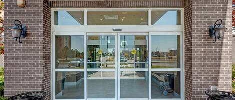 A building entrance with a glass door, brick walls, and two wall-mounted light fixtures.