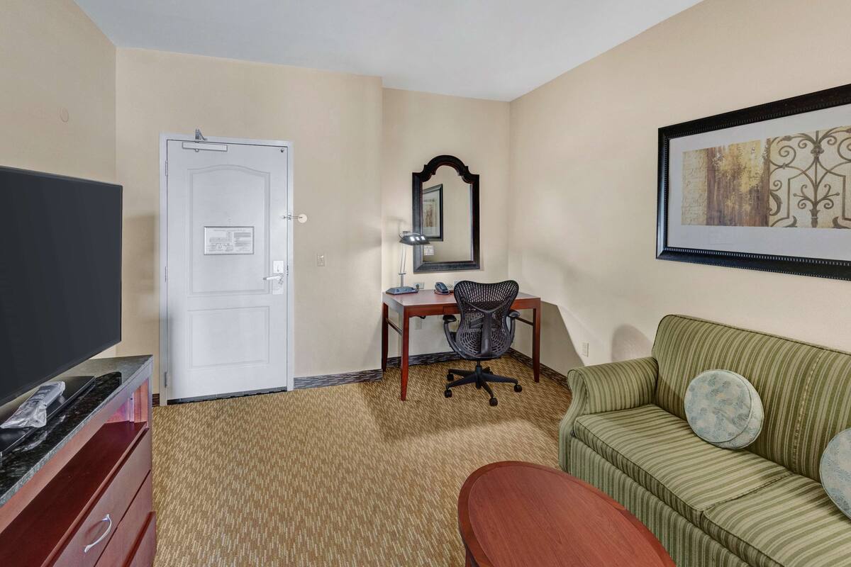 Une chambre d’hôtel équipée d’un téléviseur à écran plat, d’un bureau avec une chaise, d’un canapé à rayures vertes et d’une œuvre d’art encadrée accrochée au mur.