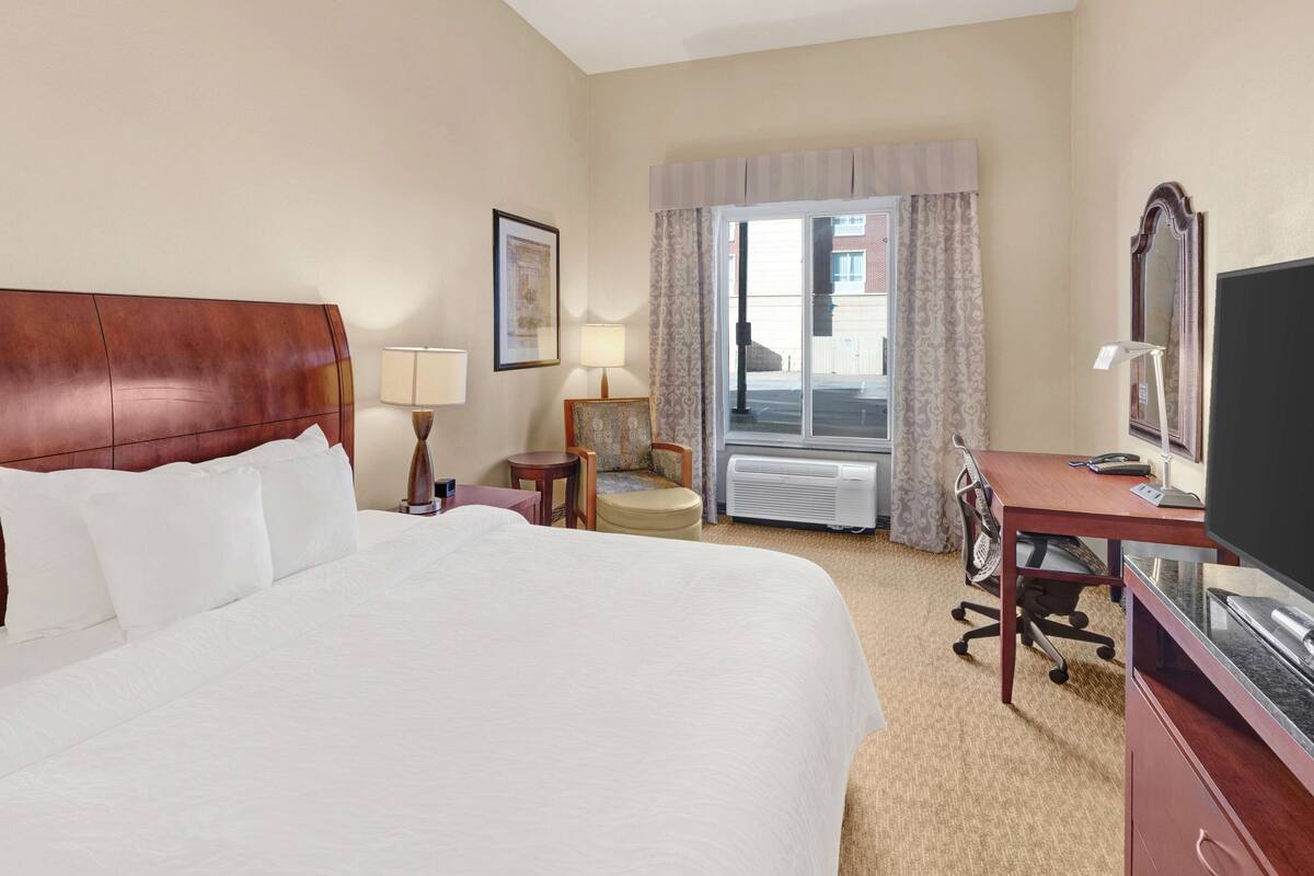 Une chambre d’hôtel avec un grand lit, un bureau avec un ordinateur, une chaise, une télévision et une fenêtre avec des rideaux.