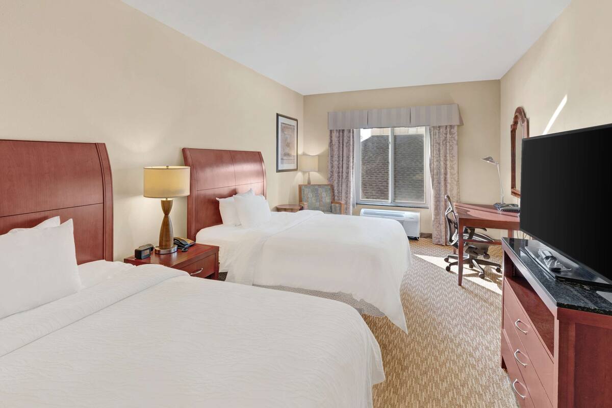 Une chambre d’hôtel avec deux lits, un bureau, une télévision et une fenêtre avec des rideaux.