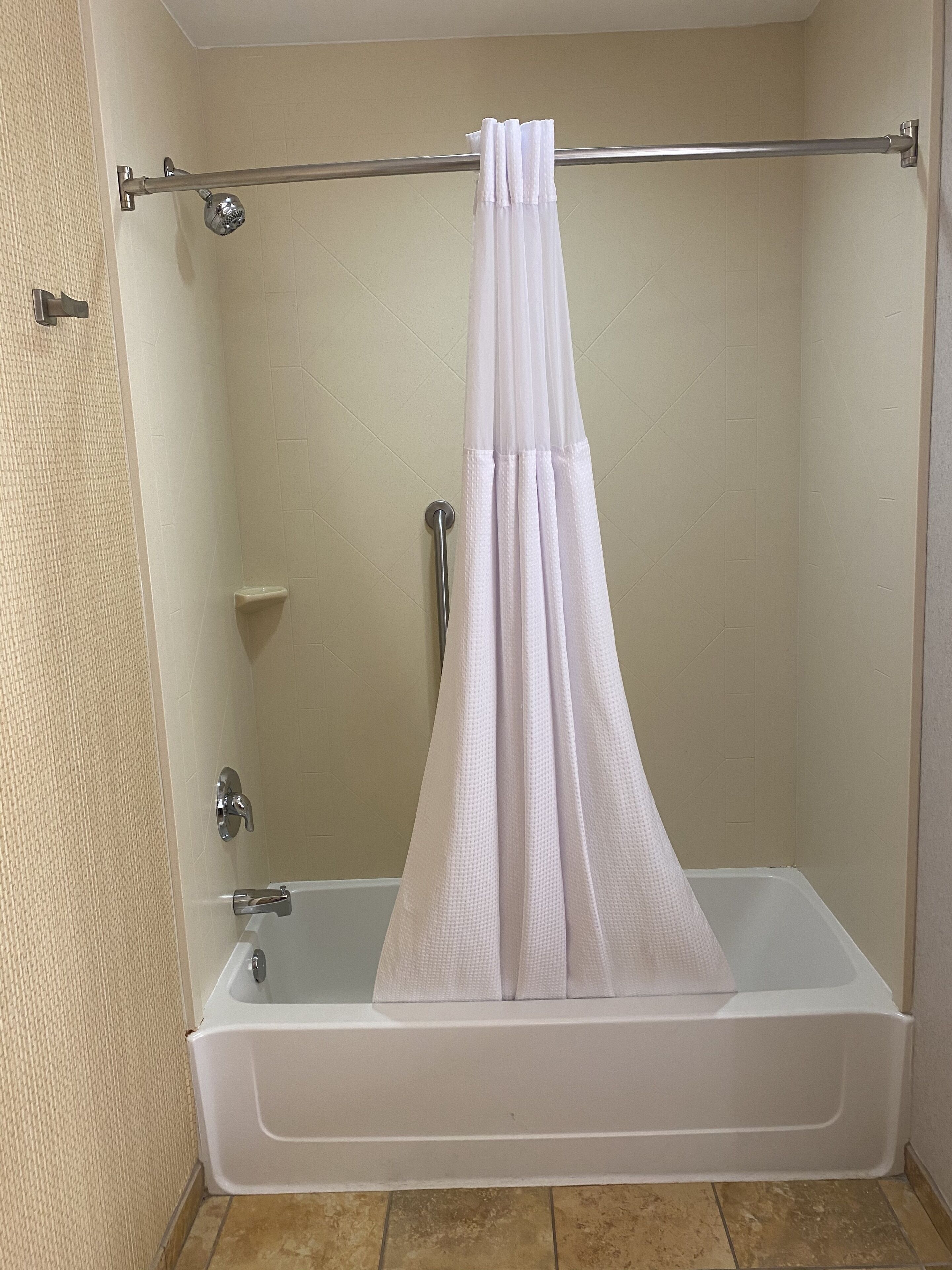 Un espace douche standard comprenant une baignoire, une tringle pour rideau de douche et un pommeau de douche.