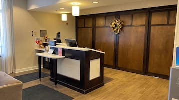 Una zona d'e recepció amb un taulell, un ordinador i un telèfon. Hi ha una paret de fusta amb una corona decorativa i un quadre penjat.