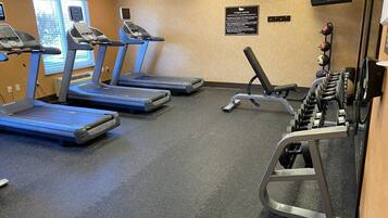 Un gimnasio con cintas de correr, una banca de pesas y un televisor montado en la pared.