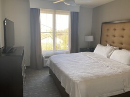 Habitación de hotel con una cama grande, un televisor en una cómoda, una ventana con cortinas y un ventilador de techo.