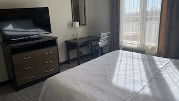 Habitación de hotel con cama, escritorio, silla, televisor y ventana con cortinas.