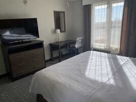 Habitación de hotel con cama, escritorio, silla, televisor y ventana con cortinas.