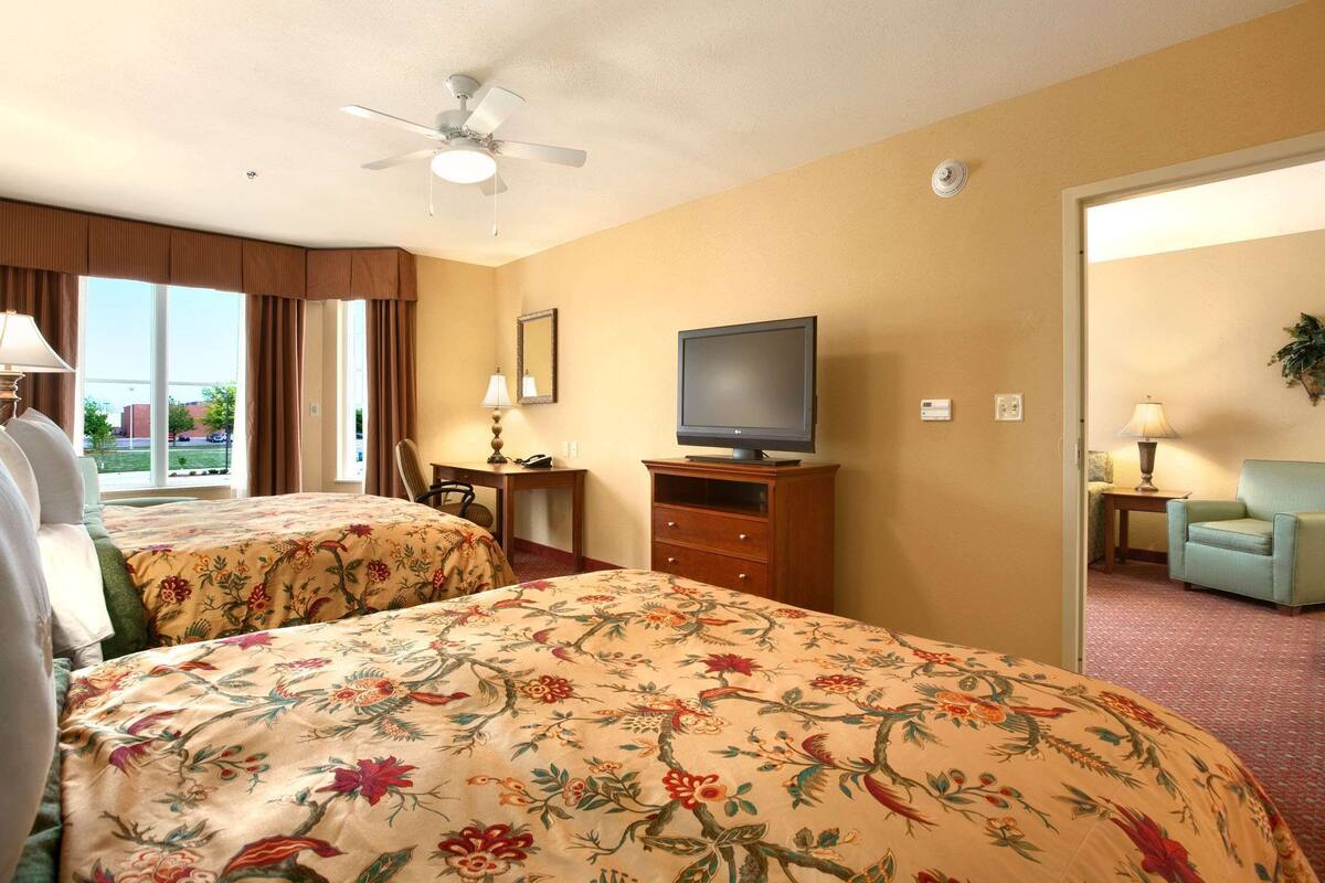 A hotel room with two beds, a television, a ceiling fan, and a view of the outdoors.