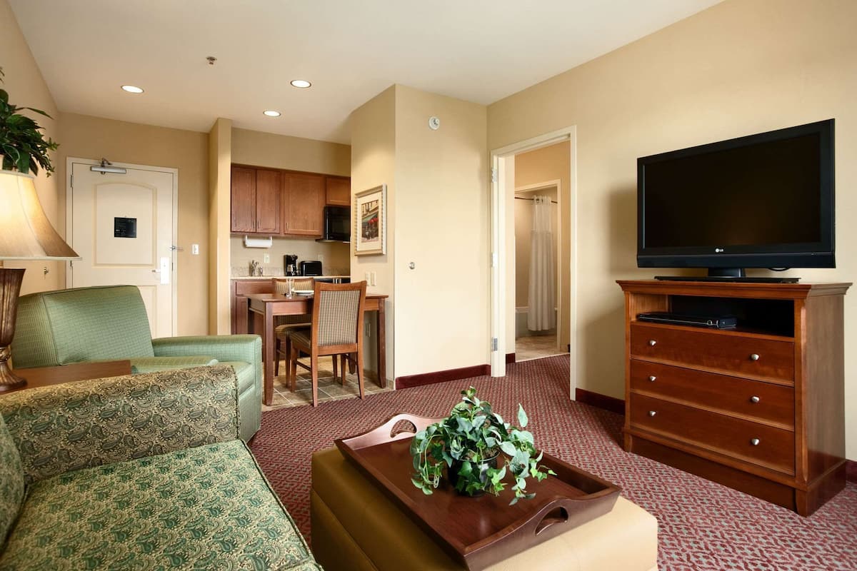 A hotel room with a living area, a dining table, a kitchenette, and a television.