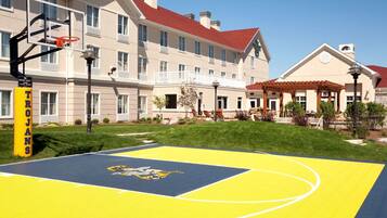 Una cancha de baloncesto con aro, un edificio con techo rojo y un letrero que dice 'SPORT COURT'.