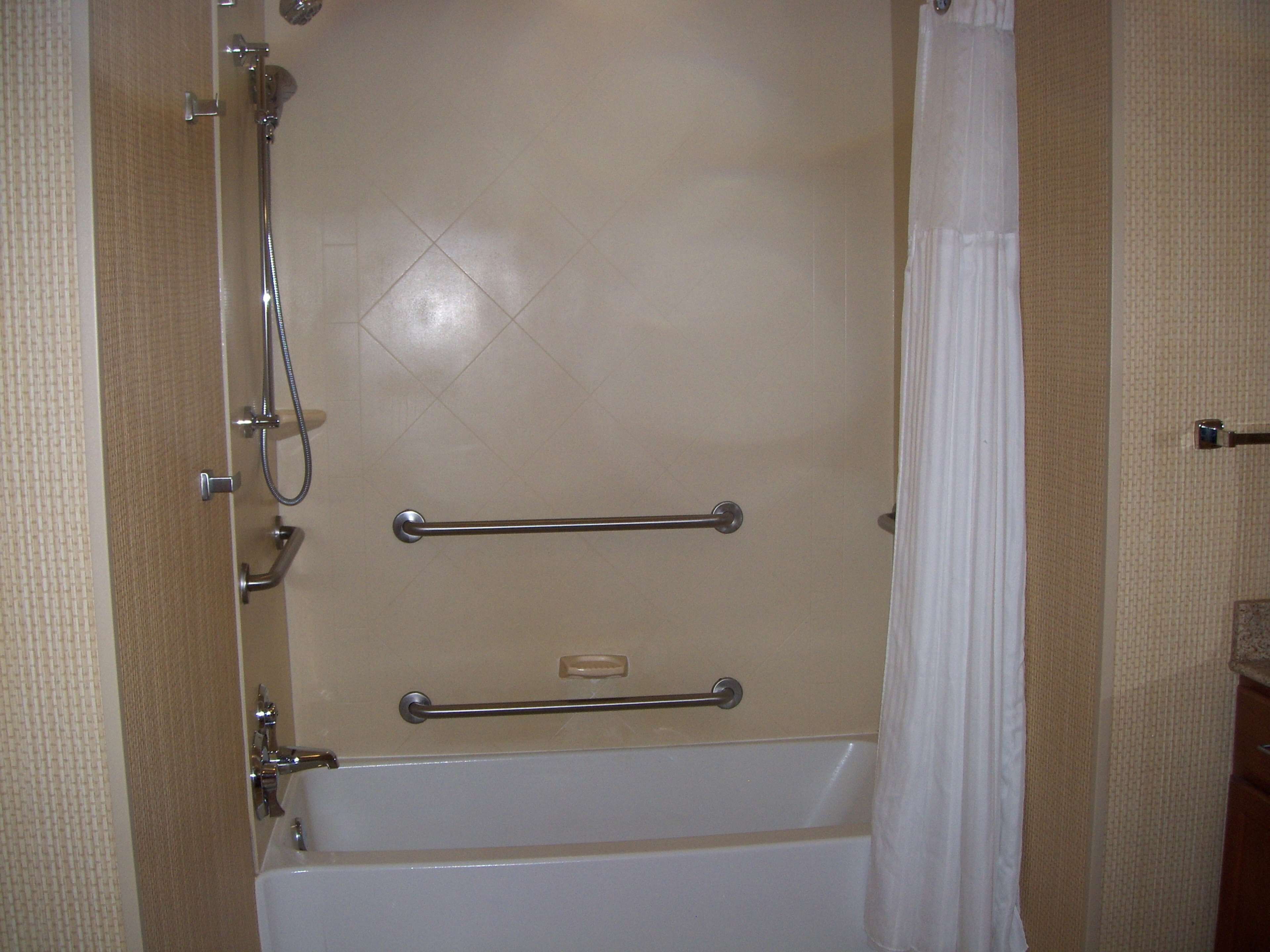 A shower with a glass door, a handheld showerhead, and a grab bar.