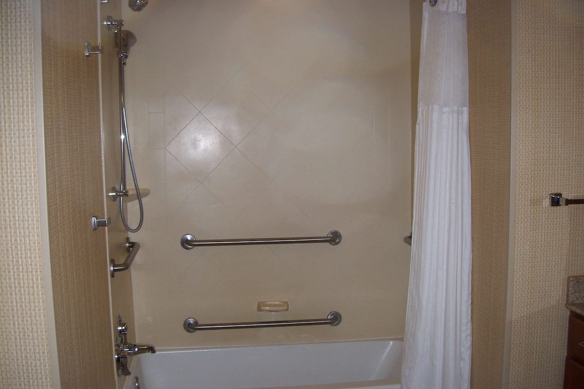 A shower with a glass door, a handheld showerhead, and a grab bar.