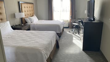 A hotel room with two beds, a desk, a chair, a television, and a window with curtains.