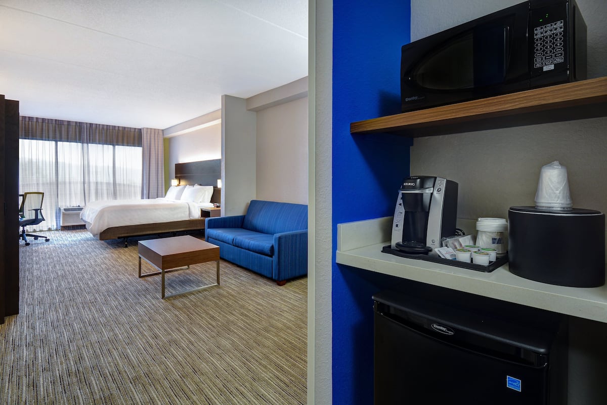 A hotel room with a bed, a blue sofa, a coffee machine, and a microwave on a shelf.