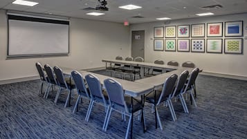 A conference room with a long table, chairs, a projector screen, and framed artwork on the walls.