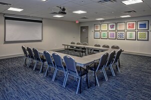 Un salón de conferencias con una larga mesa, sillas, una pantalla de proyector y cuadros en las paredes.