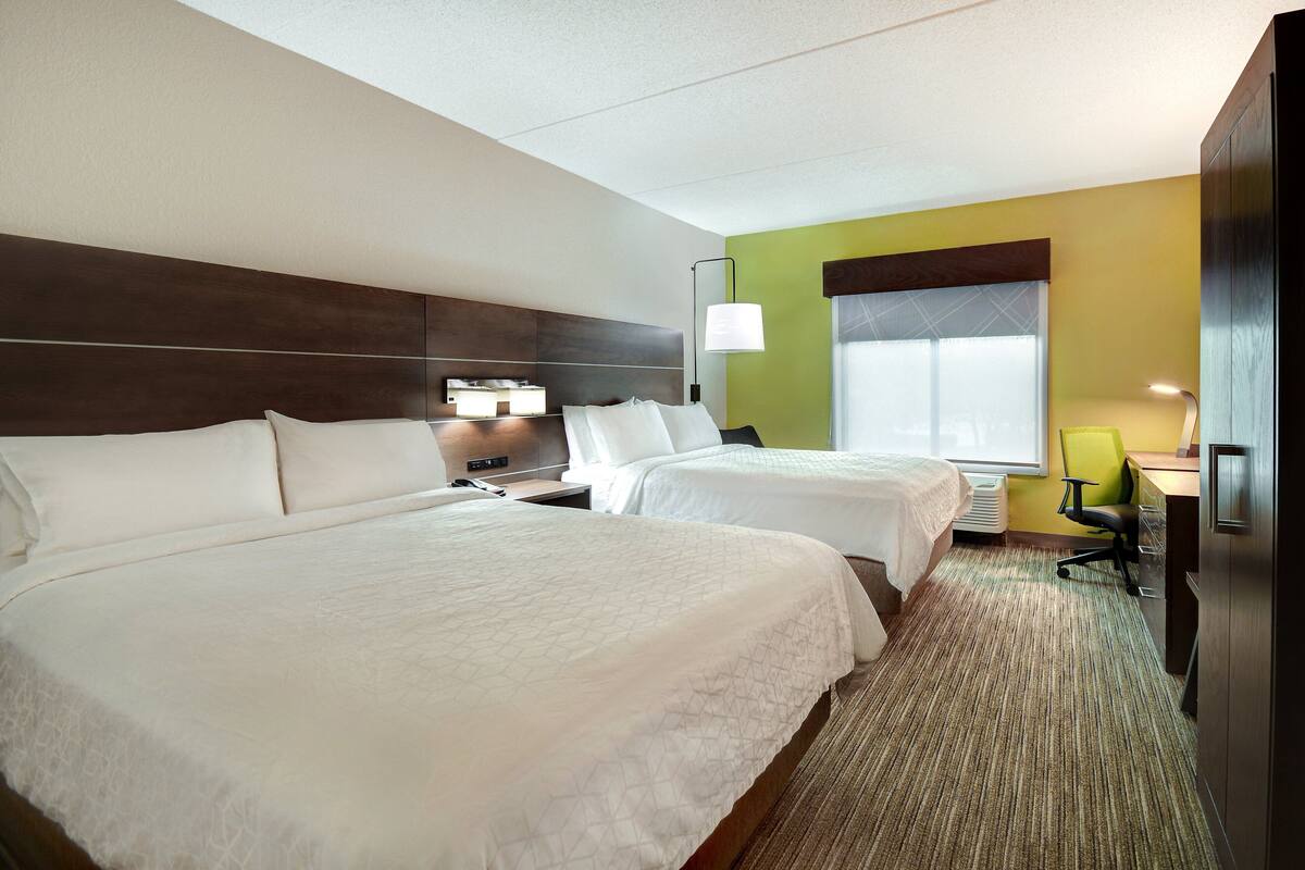 A hotel room with two beds, a desk, a chair, and a window.