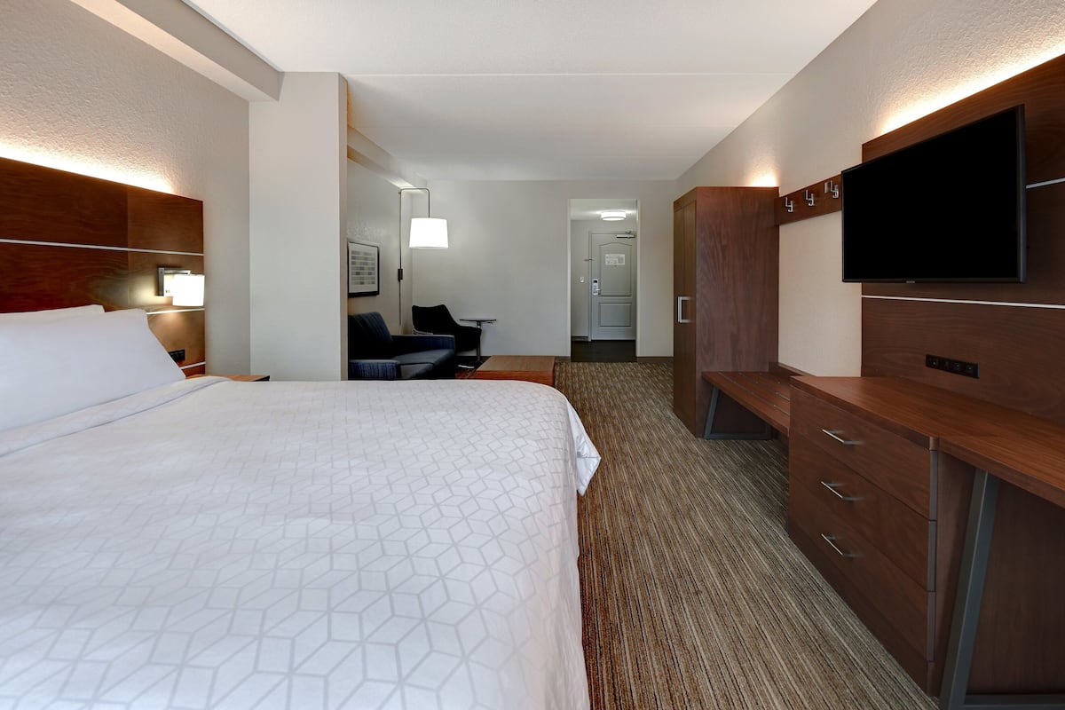 A hotel room with a large bed, a desk with drawers, a flat-screen TV, and a seating area with a chair and table.