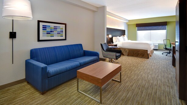 Een hotelkamer met een blauwe bank, een houten bijzettafeltje, een bed met witte lakens, een bureau met stoel en een ingelijste foto aan de muur.